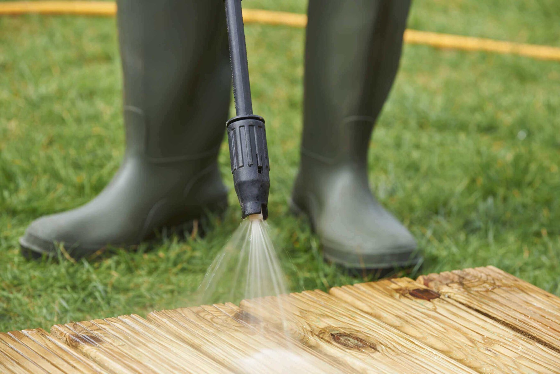 WADE BUILDING SUPPLIES | PERSON CLEANING WOODEN DECKING WEARING GREEN WELLINGTON BOOTS